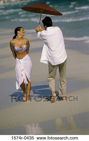 Young man holding an umbrella walking with a young woman at the beach View Large Photo Image Stock Photography - Young man holding an umbrella walking with a young woman at the beach. Fotosearch
