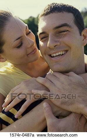 Young woman standing behind a young man with her arms around him View Large Photo Image Stock Image - Young woman standing behind a young man with her arms around him. Fotosearch