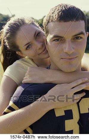 Stock Image - Young woman standing behind a young man with her arms around him. Fotosearch