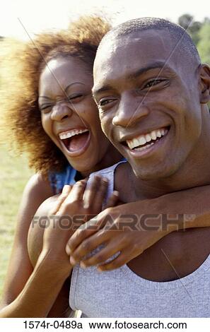 Stock Image - Young woman standing behind a young man with her arms around him. Fotosearch