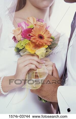 Bride and groom holding a bouquet of flowers together View Large Photo Image Picture - Bride and groom holding a bouquet of flowers together. Fotosearch