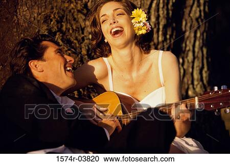 Stock Image - Bride and groom sitting together playing a guitar. Fotosearch