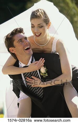 Stock Image - Bride riding piggyback on her groom. Fotosearch