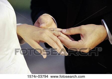 Picture - Close-up of a groom placing a ring on his bride's finger. Fotosearch