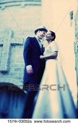 Stock Image - Low angle view of a newlywed couple standing in front of a church. Fotosearch