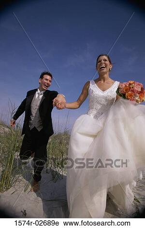Newlywed couple running on sand View Large Photo Image Stock Image - Newlywed couple running on sand. Fotosearch