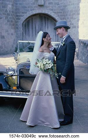 Stock Image - Newlywed couple standing in front of an antique car. Fotosearch
