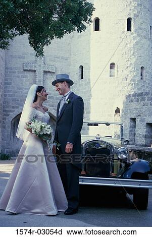 Stock Image - Newlywed couple standing in front of an antique car. Fotosearch