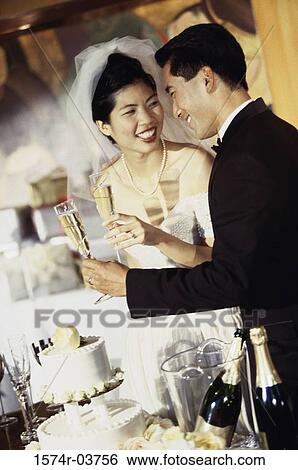 Stock Photograph - Newlywed couple standing near a wedding cake and toasting with glasses of champagne. Fotosearch
