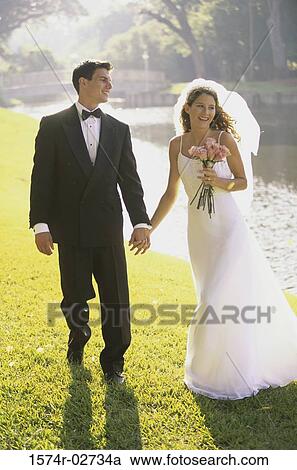 Stock Image - Newlywed couple walking together holding hands. Fotosearch