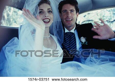 Stock Image - Newlywed couple waving from inside a car. Fotosearch