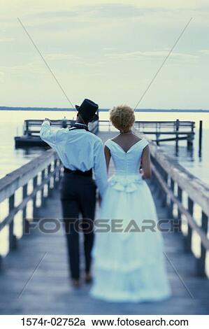 Rear view of a newlywed couple walking on a pier View Large Photo Image Stock Image - Rear view of a newlywed couple walking on a pier. Fotosearch