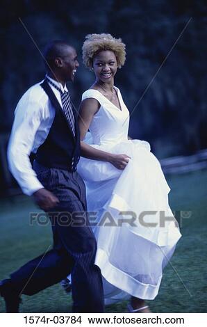 Picture - Side profile of a newlywed couple running on a lawn. Fotosearch