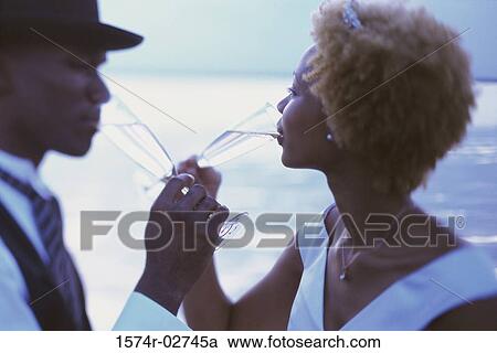 Stock Image - Side profile of a newlywed couple drinking champagne on the beach. Fotosearch