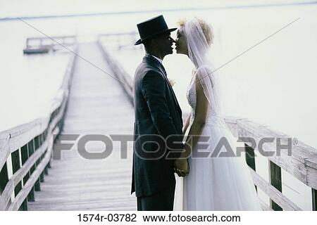 Side profile of a newlywed couple kissing on a pier View Large Photo Image Stock Image - Side profile of a newlywed couple kissing on a pier. Fotosearch