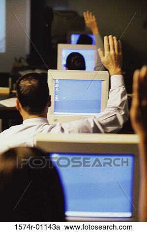 Stock Image - Business executives sitting in front of computer monitors raising their hands at a training class. Fotosearch