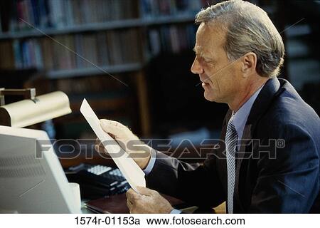 Stock Image - Businessman reading a document at his desk. Fotosearch