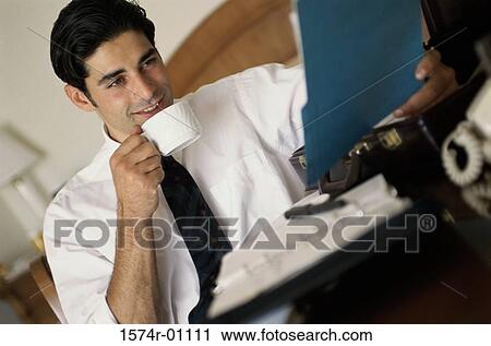 Businessman reading a file and drinking a cup of coffee View Large Photo Image Stock Image - Businessman reading a file and drinking a cup of coffee. Fotosearch