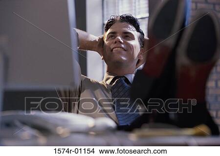 Picture - Businessman reclining in his seat with feet up on the table. Fotosearch