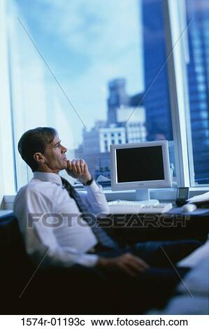Stock Image - Businessman sitting at his desk and looking out the window. Fotosearch