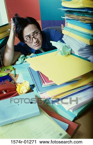 Stock Image - Businessman sitting behind a desk with stacks of files. Fotosearch