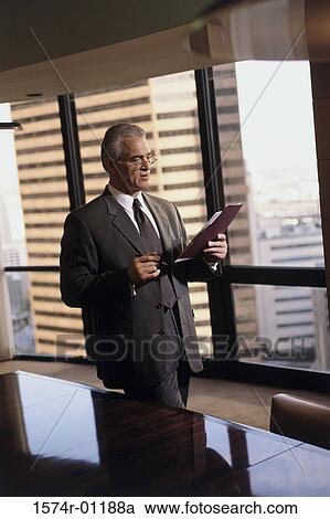 Businessman standing in a conference room and reading a file View Large Photo Image Stock Image - Businessman standing in a conference room and reading a file. Fotosearch