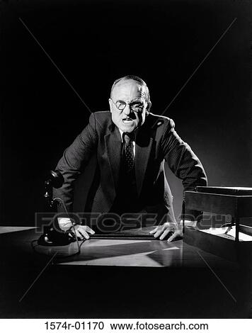 Stock Image - Businessman standing with hands on his desk. Fotosearch