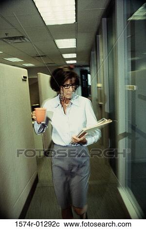 Stock Image - Businesswoman walking in a corridor holding a glass and a file. Fotosearch