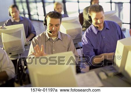 Stock Image - Group of customer service representatives sitting in front of computer monitors wearing headsets. Fotosearch