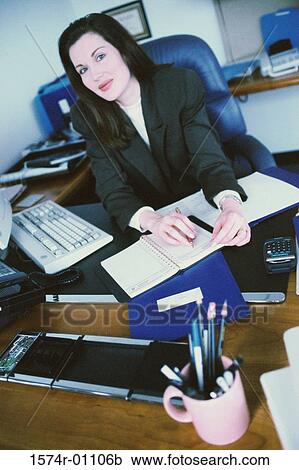 Portrait of a businesswoman seated behind a desk in an office View Large Photo Image Stock Image - Portrait of a businesswoman seated behind a desk in an office. Fotosearch