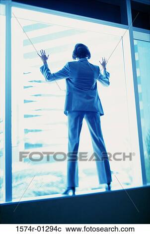 Stock Image - Rear view of a businesswoman standing on a window ledge. Fotosearch