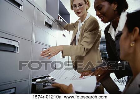 Stock Image - Two businesswomen at a filing cabinet. Fotosearch