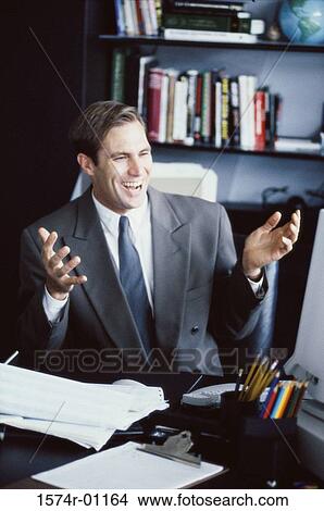 Young businessman sitting at his desk smiling View Large Photo Image Picture - Young businessman sitting at his desk smiling. Fotosearch