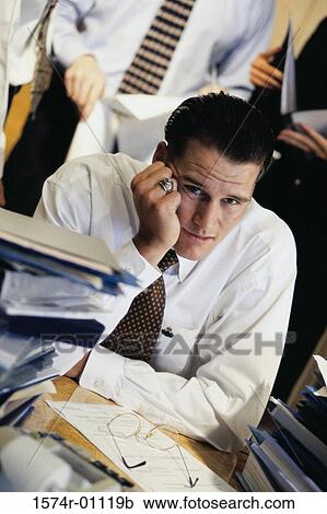 Young businessman sitting at his desk at work View Large Photo Image Stock Image - Young businessman sitting at his desk at work. Fotosearch