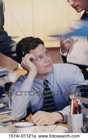 Young businessman sitting at his desk and looking up View Large Photo Image Stock Image - Young businessman sitting at his desk and looking up. Fotosearch