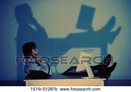 Stock Image - Young businessman talking on the landline telephone at his desk. Fotosearch