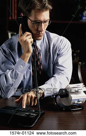 Picture - Young businessman using a landline telephone on his desk. Fotosearch