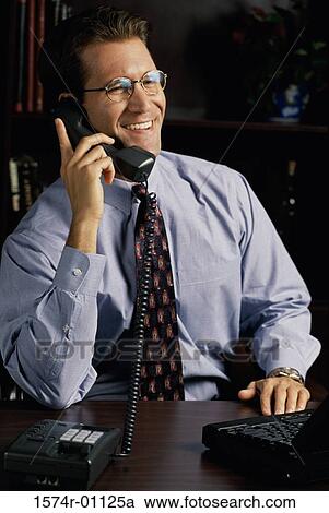 Stock Image - Young businessman using a landline telephone on his desk. Fotosearch