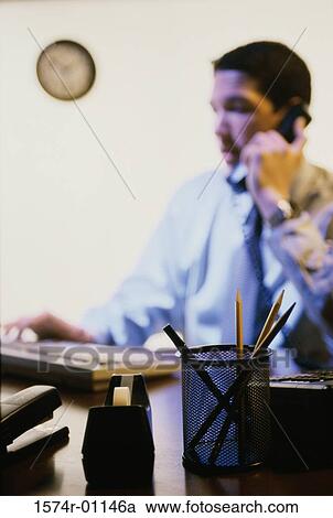 Stock Image - Young businessman using a landline telephone on his desk. Fotosearch