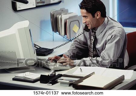 Stock Photo - Young businessman using a landline telephone on his desk. Fotosearch
