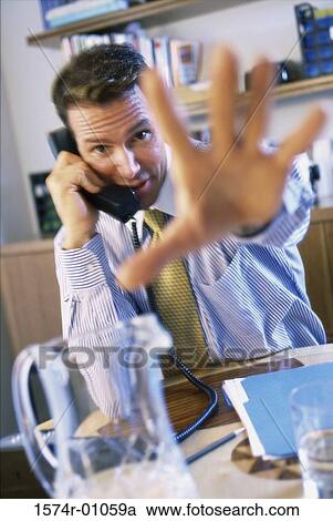 Stock Image - Young businessman using the landline telephone and holding out his palm. Fotosearch