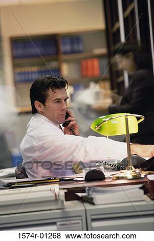 Stock Photo - Young businessman using the landline telephone at his desk. Fotosearch