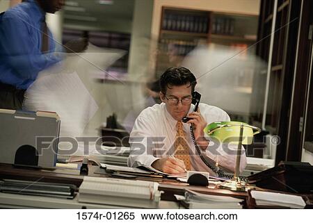 Stock Photography - Young businessman using the landline telephone at his desk. Fotosearch
