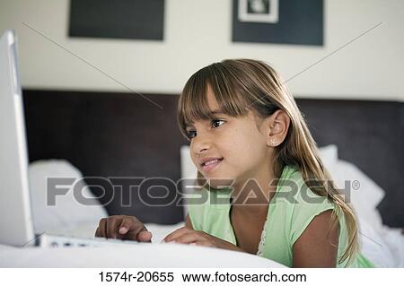 Stock Photography - Close-up of a girl lying in the bed and using a laptop. Fotosearch