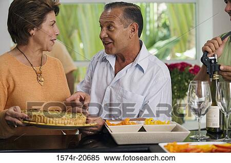 Stock Photography - Close-up of a mature couple talking to each other with a mature man unscrewing the cork of a wine bottle. Fotosearch