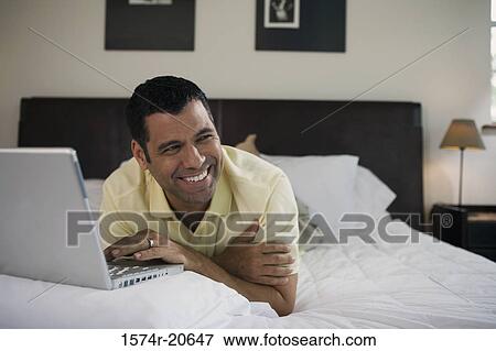 Close-up of a mature man lying in the bed and using a laptop View Large Photo Image Stock Photo - Close-up of a mature man lying in the bed and using a laptop. Fotosearch