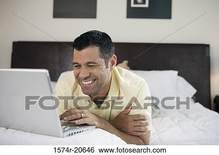 Close-up of a mature man lying in the bed and using a laptop View Large Photo Image Stock Photograph - Close-up of a mature man lying in the bed and using a laptop. Fotosearch