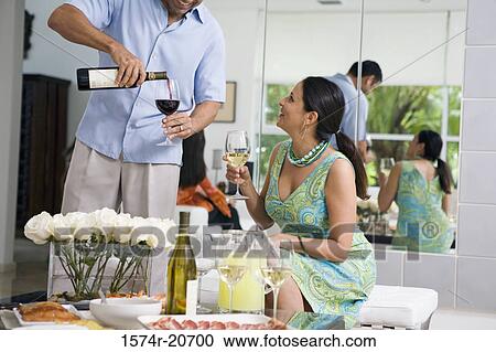Stock Image - Mature man pouring red wine into a wineglass and a mature woman looking at him. Fotosearch