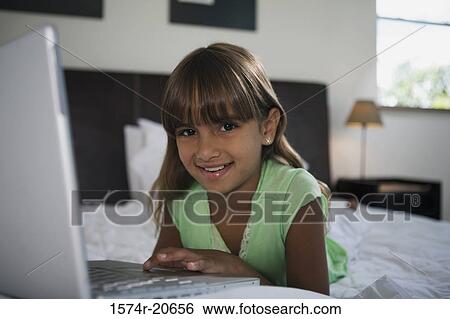 Portrait of a girl lying in the bed and using a laptop View Large Photo Image Stock Photograph - Portrait of a girl lying in the bed and using a laptop. Fotosearch