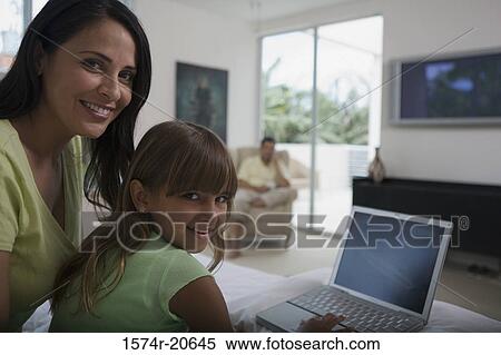 Portrait of a girl using a laptop with her mother sitting behind her View Large Photo Image Stock Photography - Portrait of a girl using a laptop with her mother sitting behind her. Fotosearch